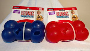 Two plastic hollow bone, blue one and a red one, with different sized holes for stuffing and dispensing treats. 