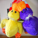 One yellow and one purple soft toy ducks both with white hair, an orange bill and orange feet with white pokkadots.