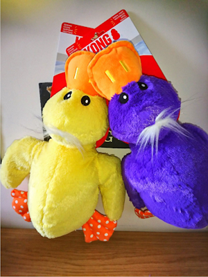 One yellow and one purple soft toy ducks both with white hair, an orange bill and orange feet with white pokkadots.